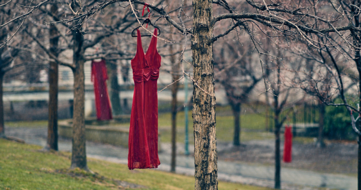 Red dresses on hangers swing from trees.
