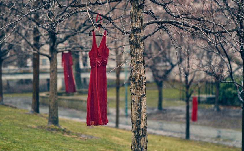 Red dresses on hangers swing from trees.