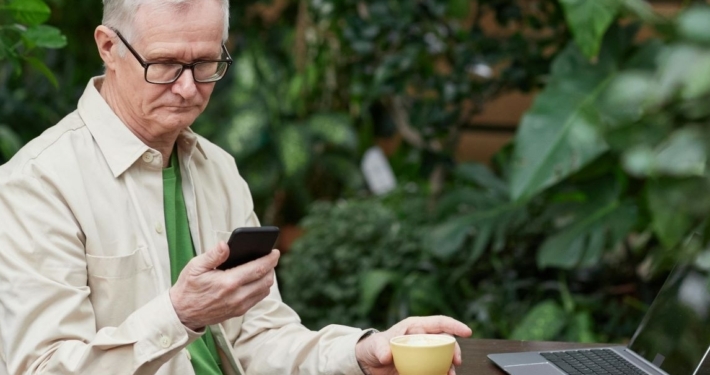 Man sitting at laptop with coffee mug checks his phone