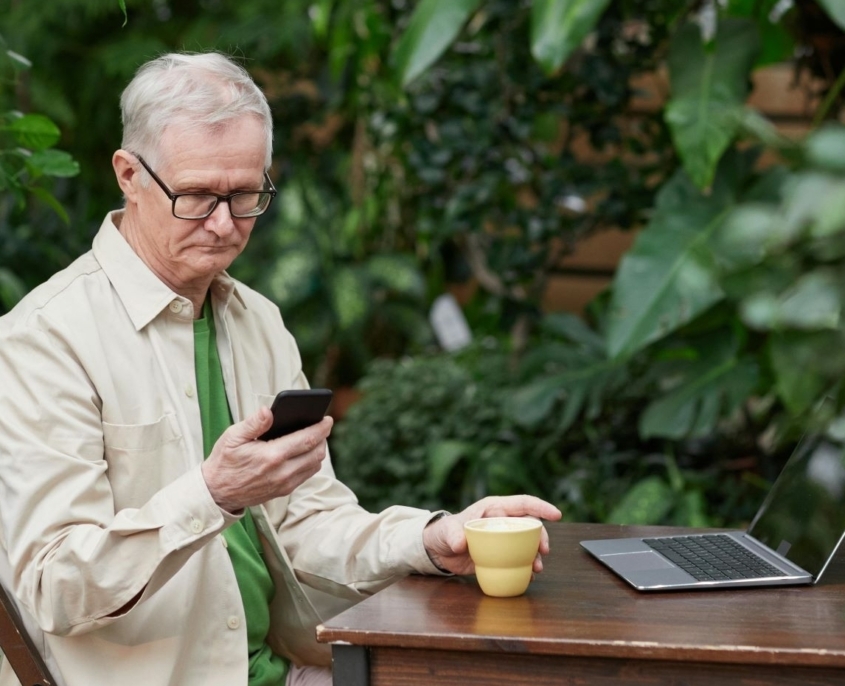 Man sitting at laptop with coffee mug checks his phone