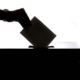 A hand drops a ballot into a ballot box in silhouette